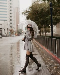 a woman is walking down the street in the rain with an umbrella and boots on