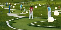 several people are playing golf in the grass with white lights on them and green hills behind them