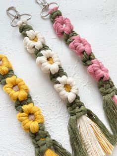 three tassels with flowers on them are hanging from metal hooks against a white wall