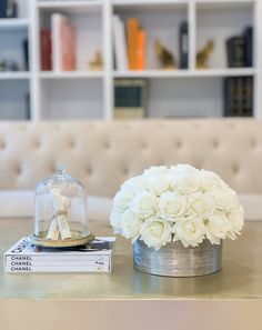 white flowers in a silver vase on a table next to books and a glass cloche