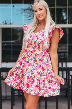 a woman in a pink floral dress posing for the camera with her hands on her hips