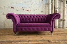 a purple couch sitting on top of a wooden floor next to a white brick wall