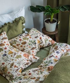 an unmade bed with green sheets and pillows on it next to a potted plant