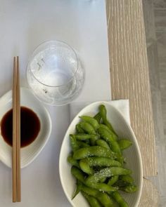 two white bowls filled with green beans next to chopsticks and a glass of water