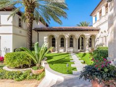 a house with palm trees in the front yard and landscaping on the side walk leading to it