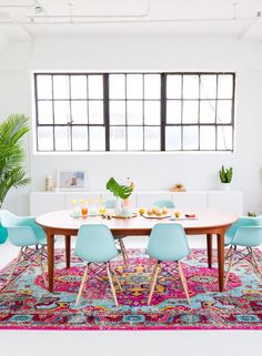 a dining room table with blue chairs and a rug on the floor in front of it