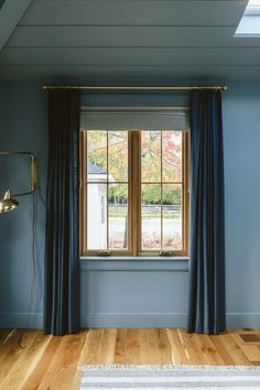 an empty room with blue walls and wood flooring is seen through the window curtains