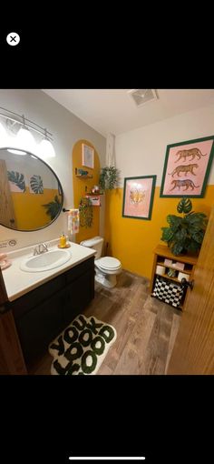 a bathroom with yellow walls and wood flooring is shown in this image, there are pictures on the wall above the toilet