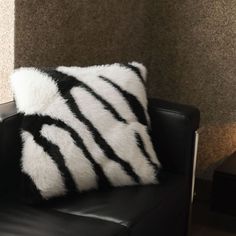 a black and white pillow sitting on top of a leather chair next to a wall