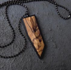 a necklace with a wooden pendant hanging from it's side on a black ball chain