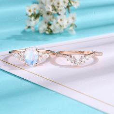 two gold rings with white stones and diamonds on a blue surface next to a bouquet of flowers