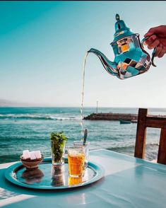 a person pouring tea on top of a plate near the ocean