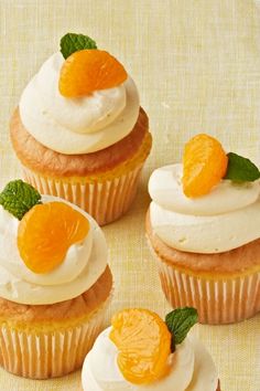 four cupcakes with white frosting, orange slices and mint leaves on top