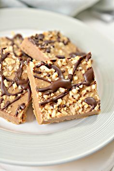 three pieces of peanut butter bars on a white plate with chocolate drizzled on top