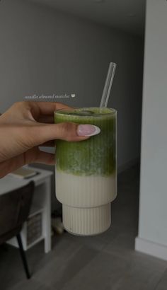 a hand holding a green drink with two straws in it's cup,