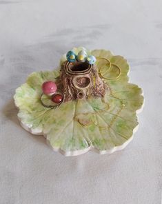 a decorative object is sitting on top of a large leafy green plate with beads and rings