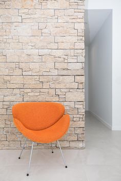 an orange chair sitting in front of a brick wall next to a white flooring