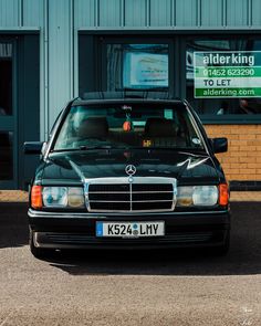 a black mercedes benz parked in front of a building with an ad for alderking on it