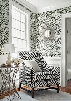 a living room decorated in black and white with leopard print on the wall, chair, mirror and table