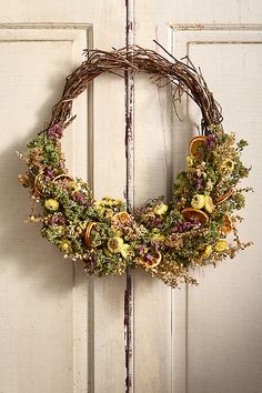 a wreath hanging on the front door of a house with dried flowers and fruit in it