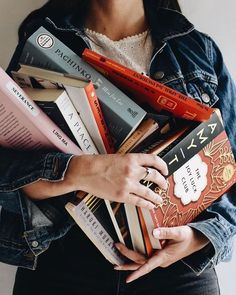 a woman is holding a bunch of books in her hands while wearing a jean jacket