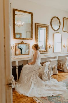 a woman in a wedding dress sitting on a chair looking at herself in the mirror