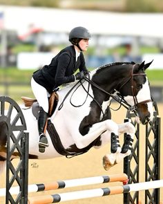 a woman riding on the back of a black and white horse jumping over an obstacle