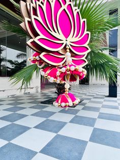 a large pink flower sculpture sitting on top of a checkerboard floor next to a palm tree