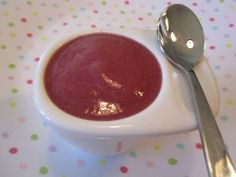 a white bowl filled with red soup and a spoon next to it on a polka dot tablecloth