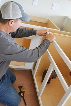 a man in grey shirt and hat working on cabinets