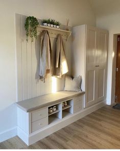 a room with white walls and wooden flooring, two coats hanging on the wall