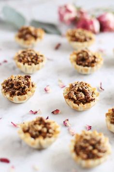 mini pies with toppings on a white marble surface next to flowers and leaves