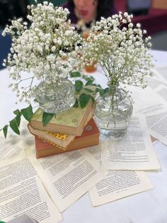 two vases filled with white flowers sitting on top of a table next to books