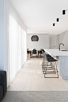 an open kitchen and dining area with white walls, wood flooring and black bar stools