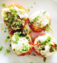 four small stuffed tomatoes on a plate with cheese and broccoli sprinkled on top