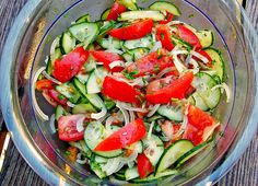 a glass bowl filled with cucumbers and tomatoes on top of a wooden table