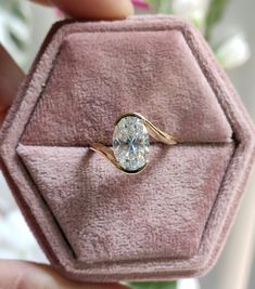 a person holding a ring in a pink velvet box with flowers on the other side