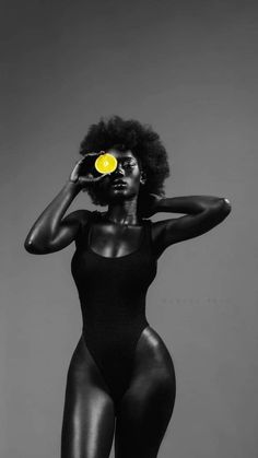 a woman in black bodysuit holding a yellow frisbee over her face and looking at the camera