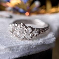 three stone diamond ring sitting on top of a white cloth covered tablecloth with a christmas tree in the background