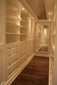 an empty walk in closet with lots of white cabinets and drawers on the wall, along with hardwood flooring