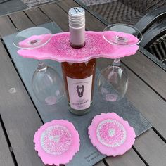 a bottle and two wine glasses sitting on a table with pink coasters in front of it