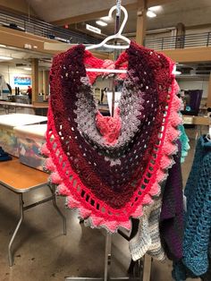 a crocheted shawl hanging from a rack in a room filled with tables and chairs