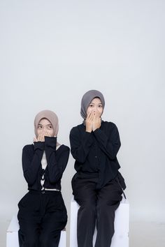 two young women sitting next to each other with their hands on their mouths while covering their faces