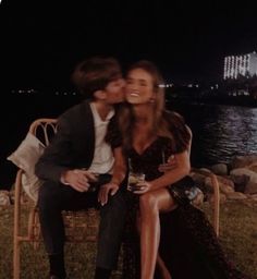 a man and woman sitting next to each other on a bench near the water at night