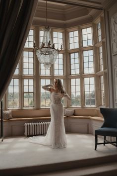 a woman standing in front of a large window wearing a wedding dress with long sleeves