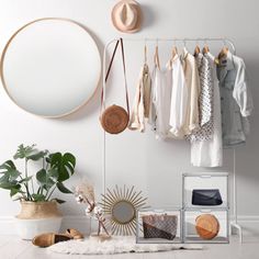 a white room with clothes and accessories hanging on the wall, including a round mirror