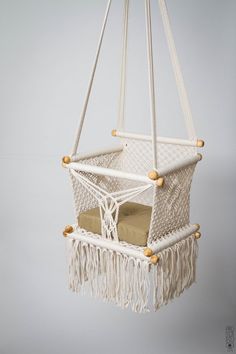 a white hammock hanging from the ceiling with red cushion and tassels