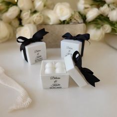 two small white candles are sitting on a table next to some flowers and a black ribbon