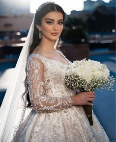 a woman in a wedding dress holding a bouquet of flowers and wearing a veil over her head