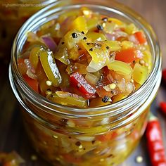 a glass jar filled with pickled vegetables on top of a wooden table next to red peppers